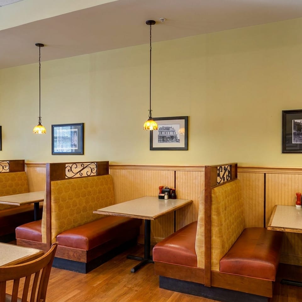 Warmly lit restaurant dining room with upholstered booths, wooden tables, framed artwork, and pendant lights.