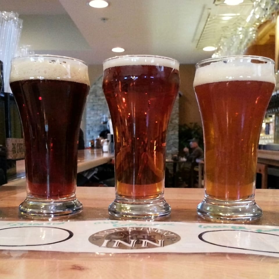 Five pint glasses of dark and amber beers sit on a wooden bar in a cozy pub.