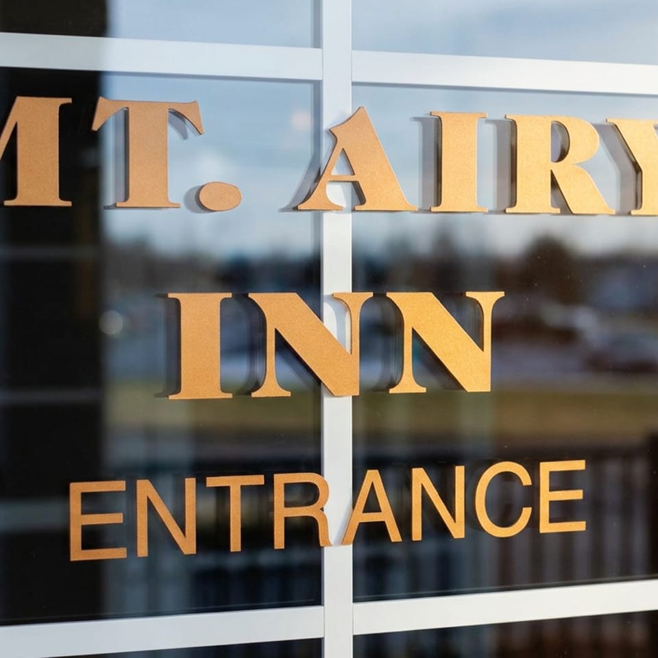 Gold lettering on a glass door reads “Mt. Airy Inn Entrance,” reflecting the outdoor surroundings.