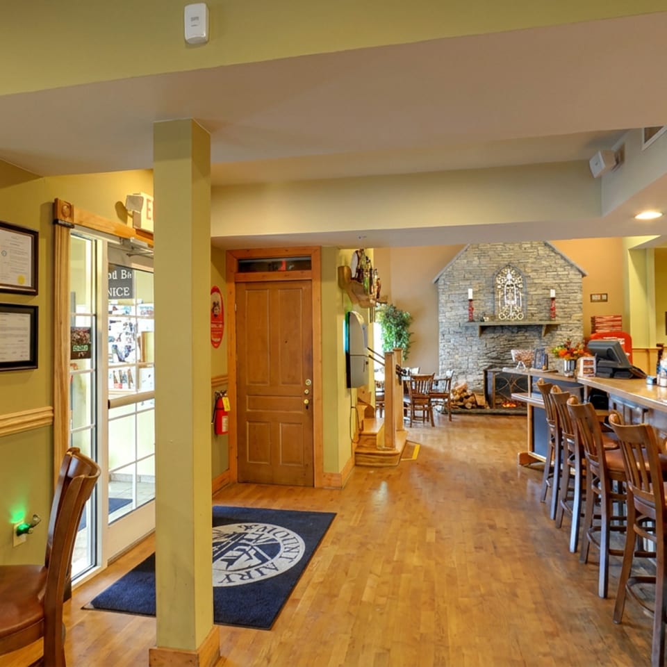 Warmly lit inn restaurant interior with a long wooden bar, high chairs, tables, stone fireplace, and Mountain Aire Inn décor.